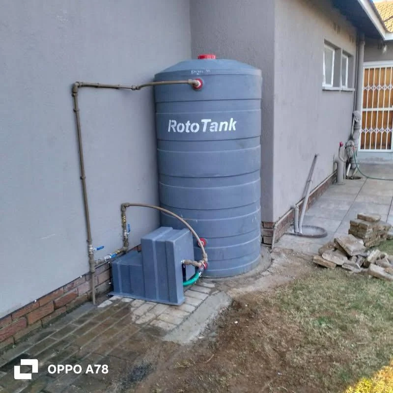 Grey water tank with connected pipework beside a residential building