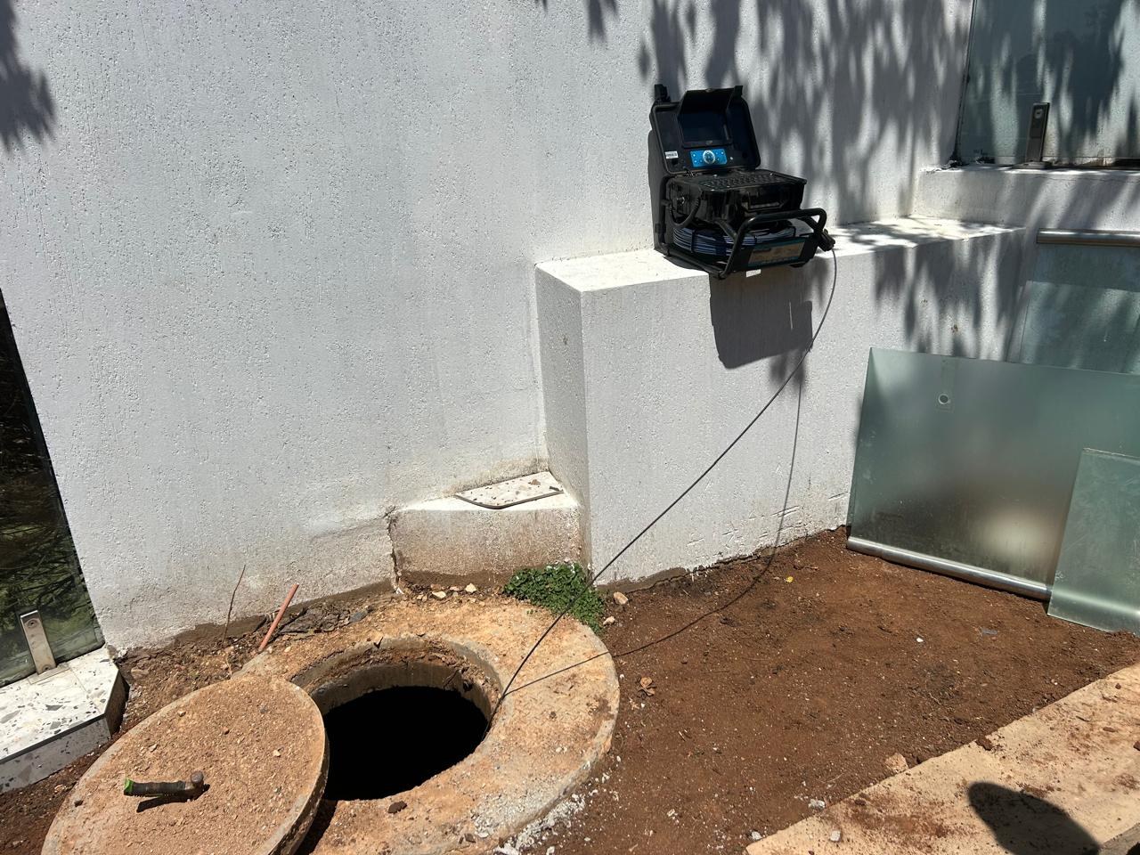 Drain camera equipment beside an open inspection chamber with its cable lowered into the drain