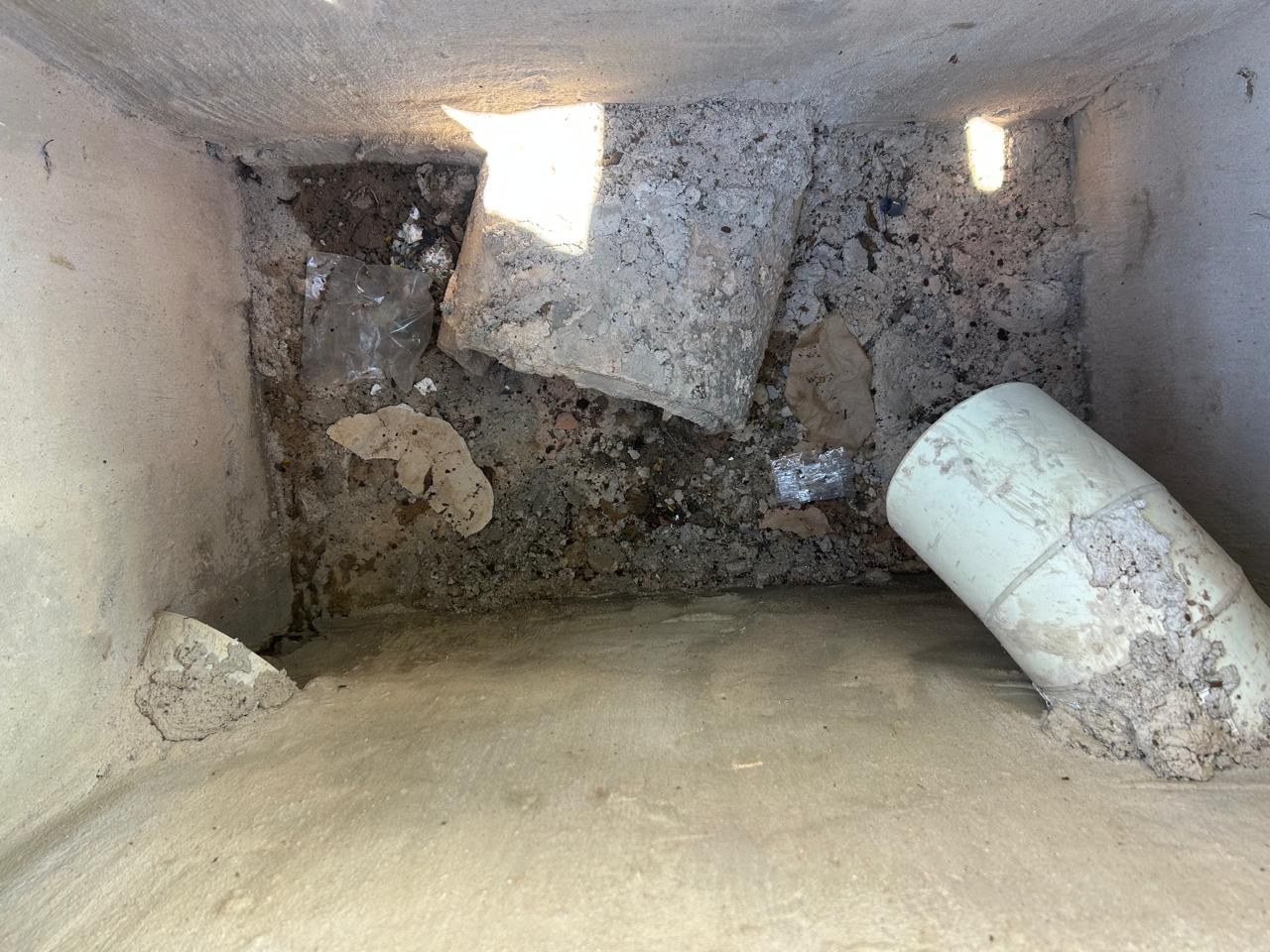 Concrete drain chamber containing rubble and debris beside a pipe opening