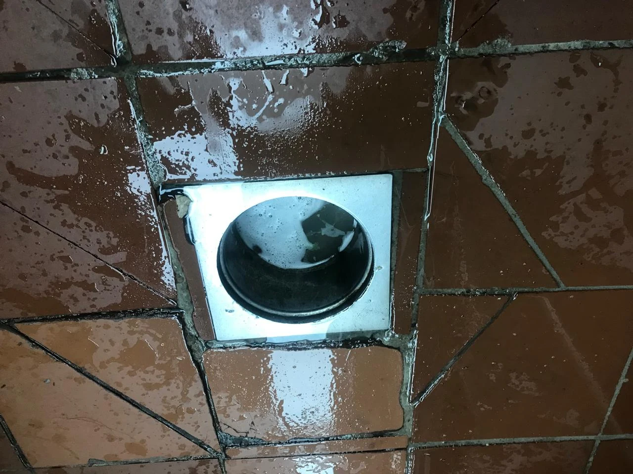 Open floor drain surrounded by wet terracotta tiles